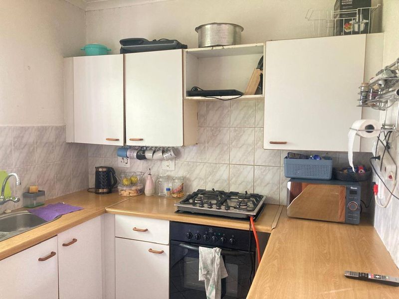A compact kitchen featuring laminate countertops, built-in cabinetry, a gas hob, and an integrated oven, requiring cosmetic updates to modernize the space.