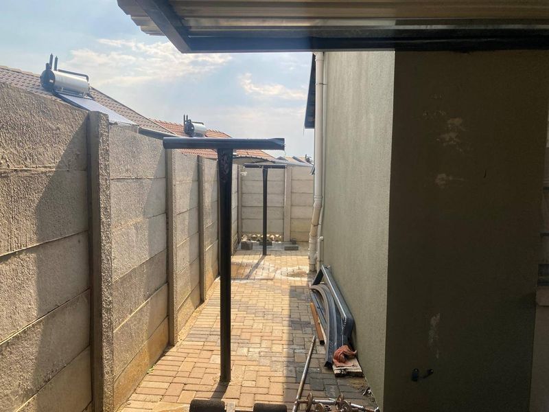 A narrow side passage featuring paved flooring, precast concrete boundary walls, and fixed metal washing line poles.