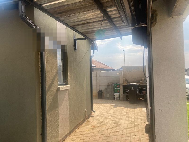 A covered outdoor patio area featuring paved flooring and a built-in braai, requiring some maintenance to the exterior wall and roof structure.