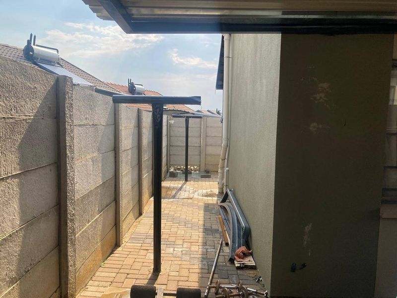 A side exterior walkway featuring paved flooring, precast concrete boundary walls, and a solar water heating system installed on the roof.