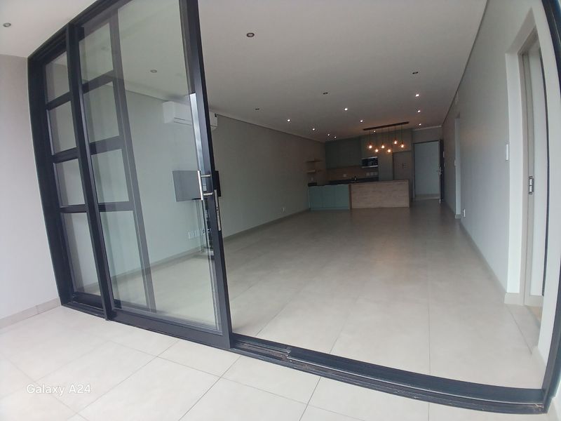 Spacious open-plan living area featuring modern kitchen cabinetry, an island, tiled flooring, and large sliding glass doors leading to an outdoor space.