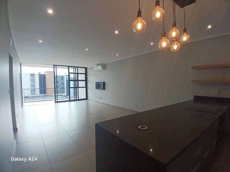 Modern open-plan living area featuring tiled floors, recessed lighting, a sleek kitchen island, and sliding doors leading to a balcony.