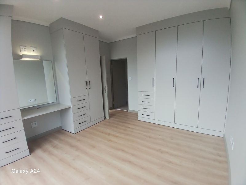 A spacious, modern bedroom featuring extensive built-in cabinetry, a dedicated vanity area, and light-toned laminate flooring in excellent condition.