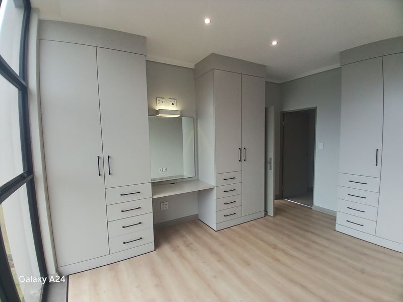 A modern bedroom featuring extensive built-in cabinetry with an integrated vanity station, light wood-look laminate flooring, and recessed ceiling lighting.