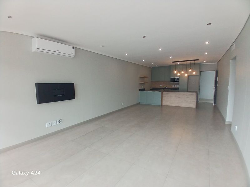 Spacious open-plan living area featuring modern kitchen cabinetry, a central island, wall-mounted fireplace, air conditioning, and neutral tiled flooring throughout.