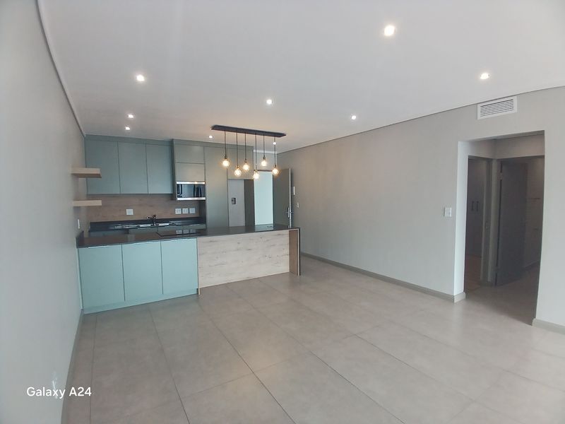 Modern open-plan kitchen and living area featuring sleek cabinetry, stone countertops, integrated appliances, and neutral tiled flooring throughout.