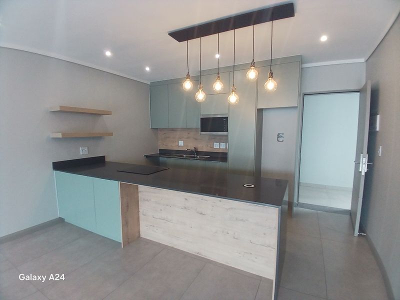 Modern kitchen featuring sleek cabinetry, stone countertops, integrated hob, built-in microwave, and stylish pendant lighting, set against neutral tiled flooring.