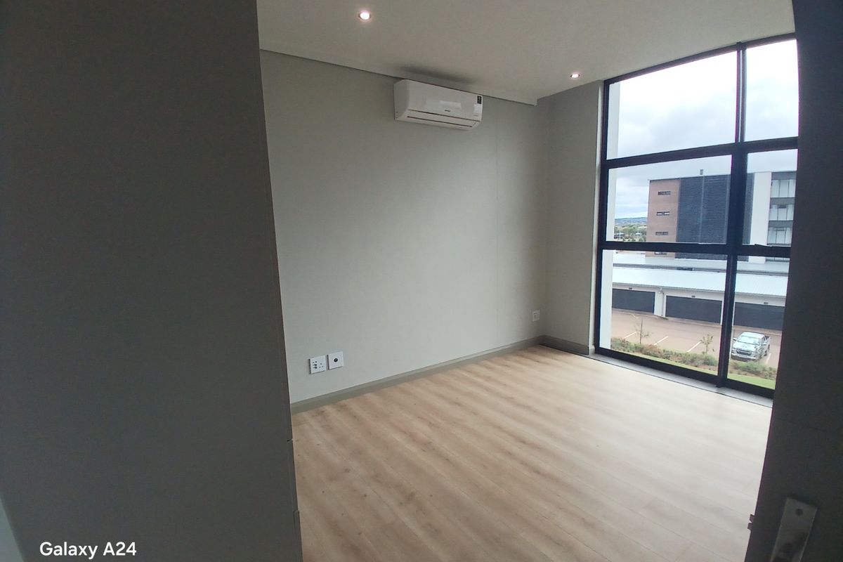 A bright, empty bedroom featuring modern laminate flooring, a wall-mounted air conditioning unit, and large floor-to-ceiling windows with natural light.