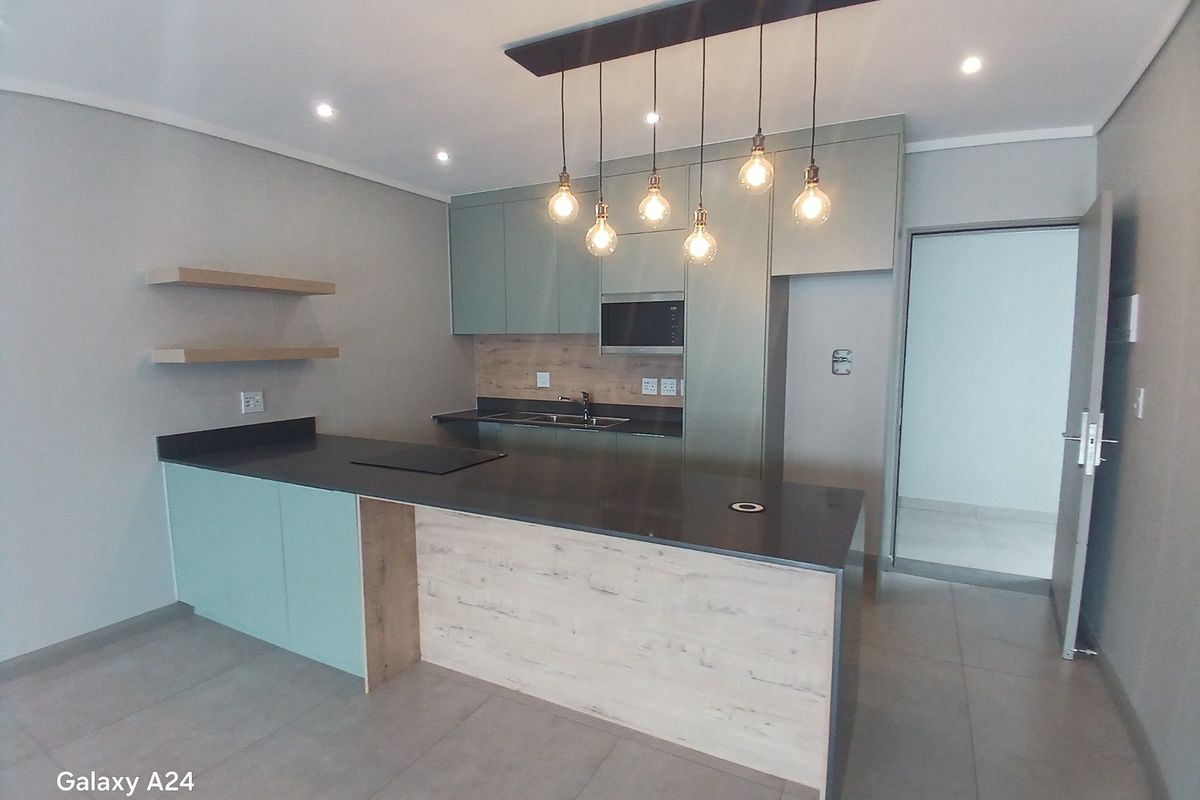 Modern kitchen featuring sleek cabinetry, stone countertops, integrated hob, built-in microwave, and stylish pendant lighting, set against neutral tiled flooring.
