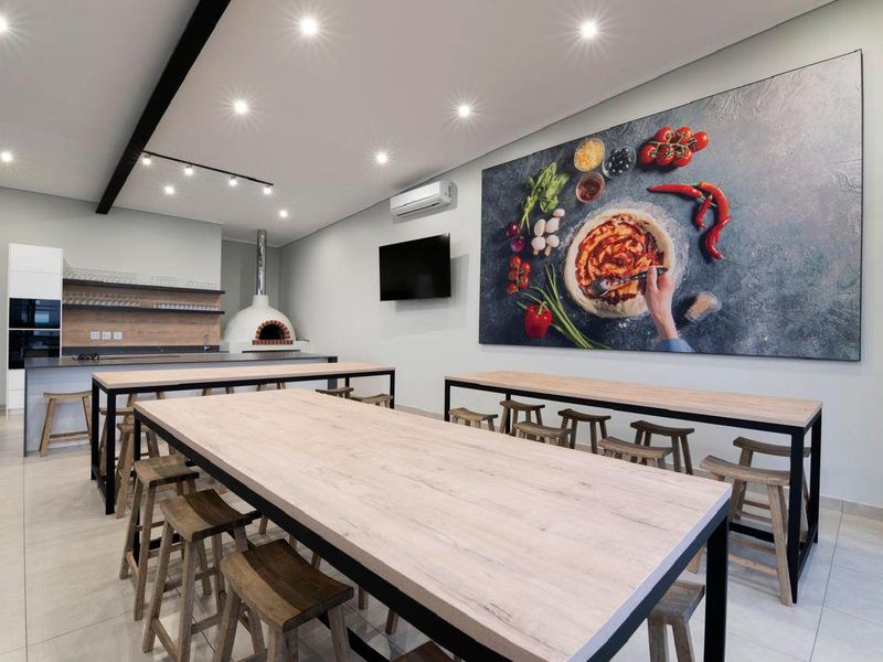 Modern open-plan entertainment area featuring a built-in pizza oven, sleek kitchen cabinetry, recessed lighting, and tiled flooring, ideal for social gatherings.