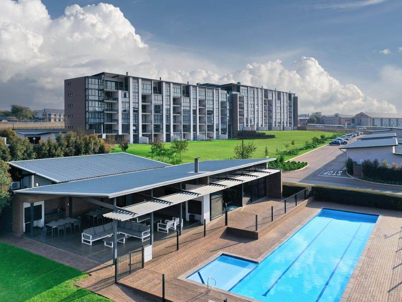 Aerial view of a modern apartment complex featuring a communal swimming pool, paved deck, and a covered outdoor entertainment area.
