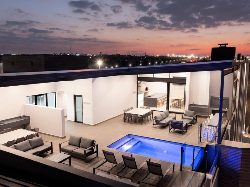 Spacious rooftop terrace featuring a modern swimming pool, built-in braai area, and outdoor kitchen, offering expansive city views at sunset.