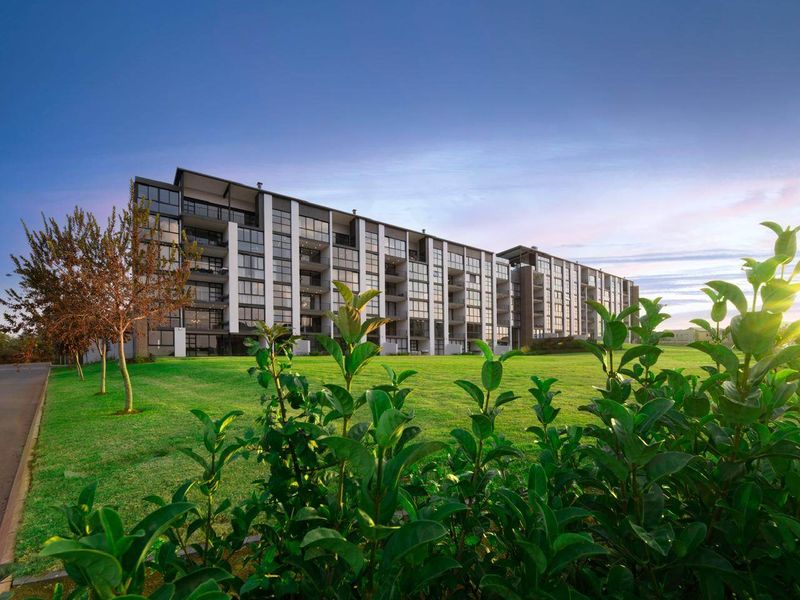 A modern multi-story apartment building featuring extensive glass balconies and a well-maintained lawn area under a clear sky.