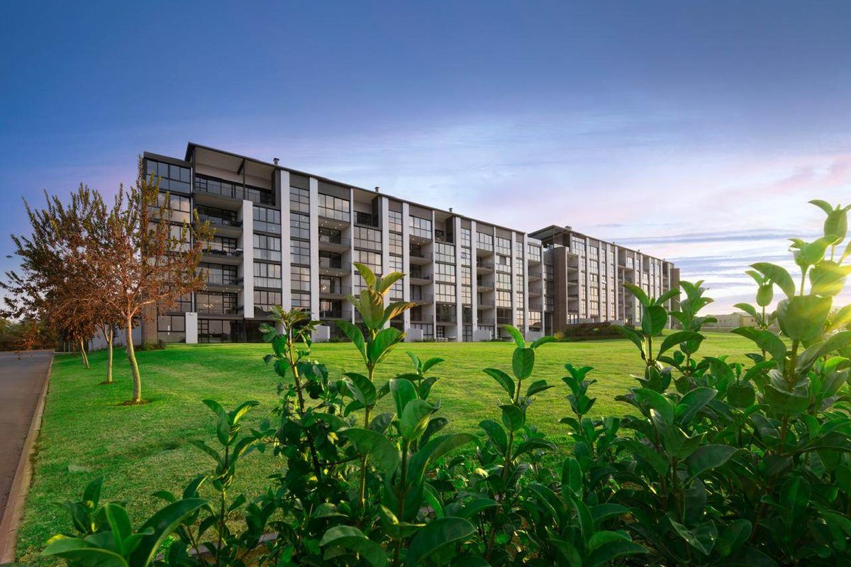 A modern multi-story apartment building featuring extensive glass balconies and a well-maintained lawn area under a clear sky.