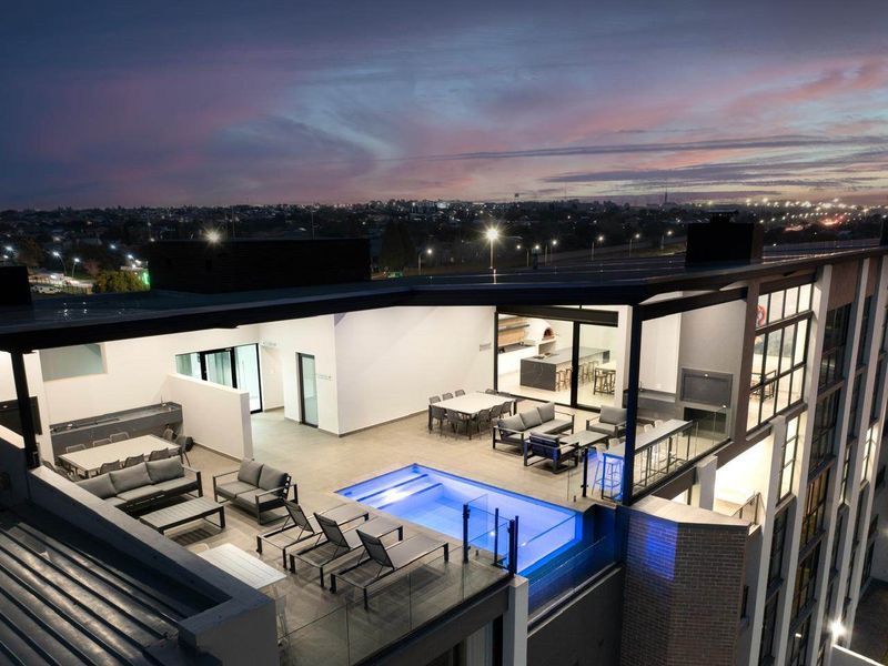 Aerial view of a luxury apartment rooftop terrace featuring a swimming pool, outdoor entertainment area, and modern architectural finishes at dusk.
