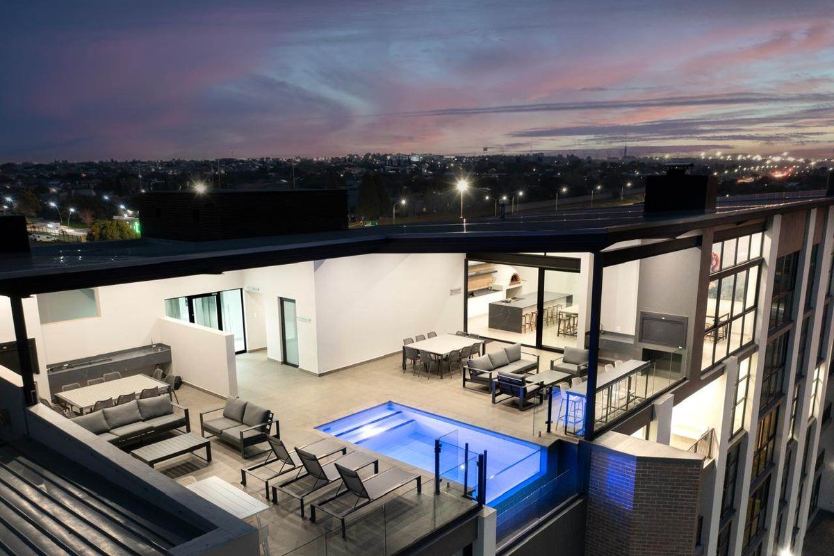 Aerial view of a luxury apartment rooftop terrace featuring a swimming pool, outdoor entertainment area, and modern architectural finishes at dusk.
