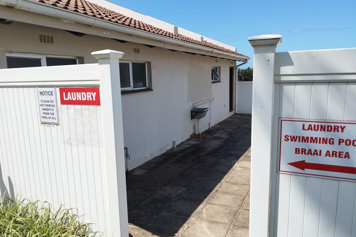 Exterior rear view of the apartment building showing a paved walkway, external utility sink, and directional signage for communal facilities.