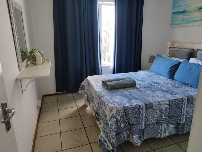 A functional bedroom featuring tiled flooring and a wall-mounted shelf, providing a simple and practical sleeping space.