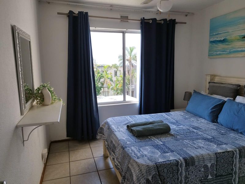 A bedroom featuring tiled flooring, a ceiling fan, and a sliding window with views of the surrounding complex.