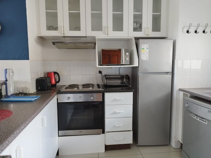 Compact kitchen featuring white cabinetry, built-in oven, electric hob, extractor fan, and tiled backsplash with ample storage space.