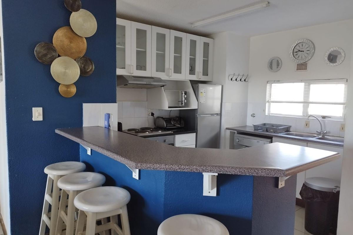 A functional kitchen featuring a breakfast bar, built-in cabinetry, integrated hob and oven, and a stainless steel sink with a tiled backsplash.