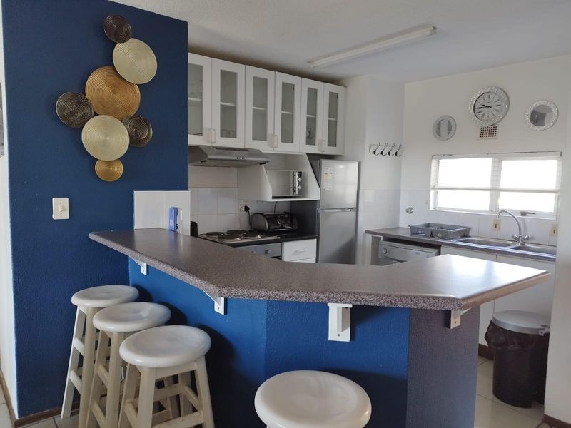 A functional kitchen featuring a breakfast bar, built-in cabinetry, integrated hob and oven, and a stainless steel sink with a tiled backsplash.
