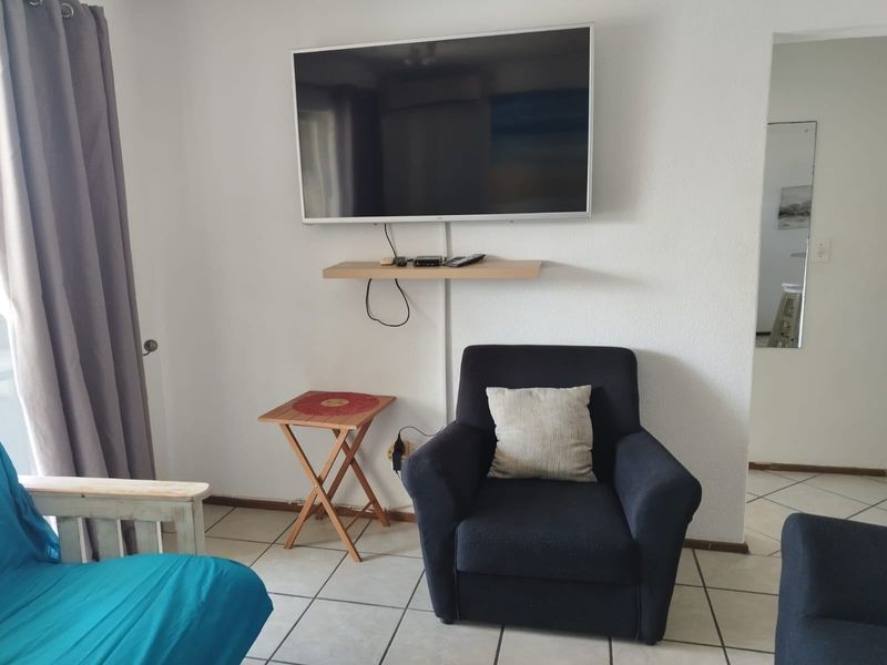 A living area featuring ceramic floor tiles, a wall-mounted television, and a floating shelf, providing a functional space for relaxation.