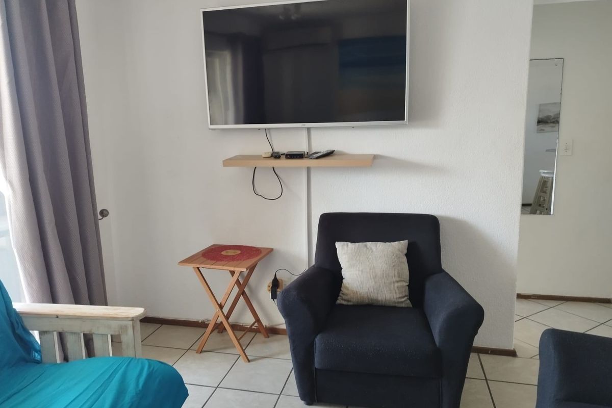 A living area featuring ceramic floor tiles, a wall-mounted television, and a floating shelf, providing a functional space for relaxation.