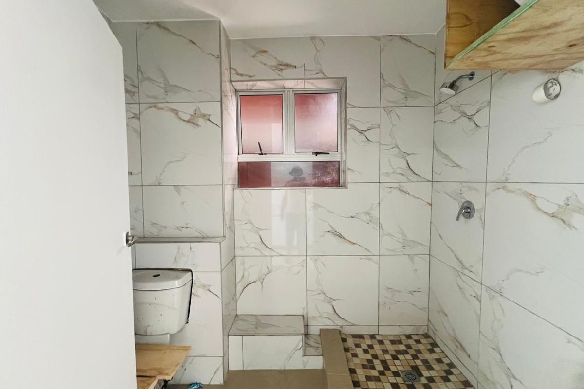 A bathroom featuring marble-look wall tiles, a walk-in shower area with mosaic floor tiles, and a window for natural light.
