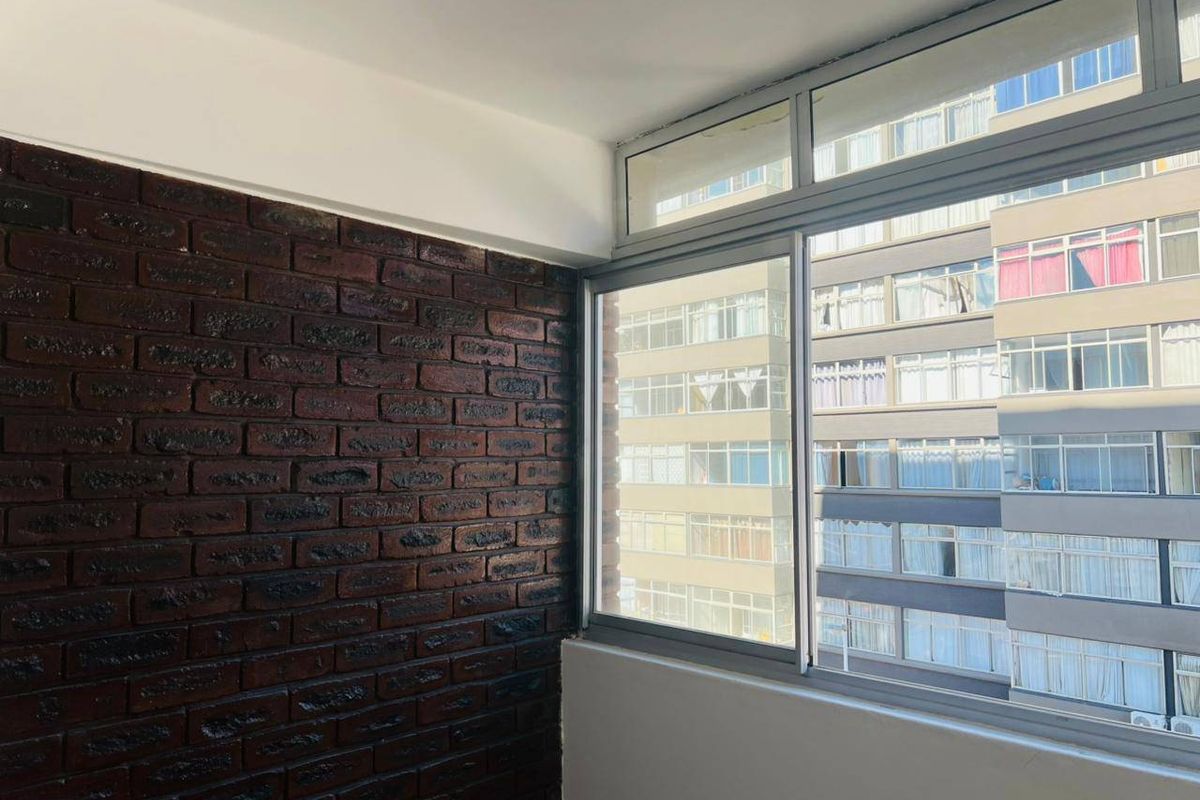 A bright interior space featuring a dark brick accent wall and large sliding windows overlooking the surrounding apartment complex.