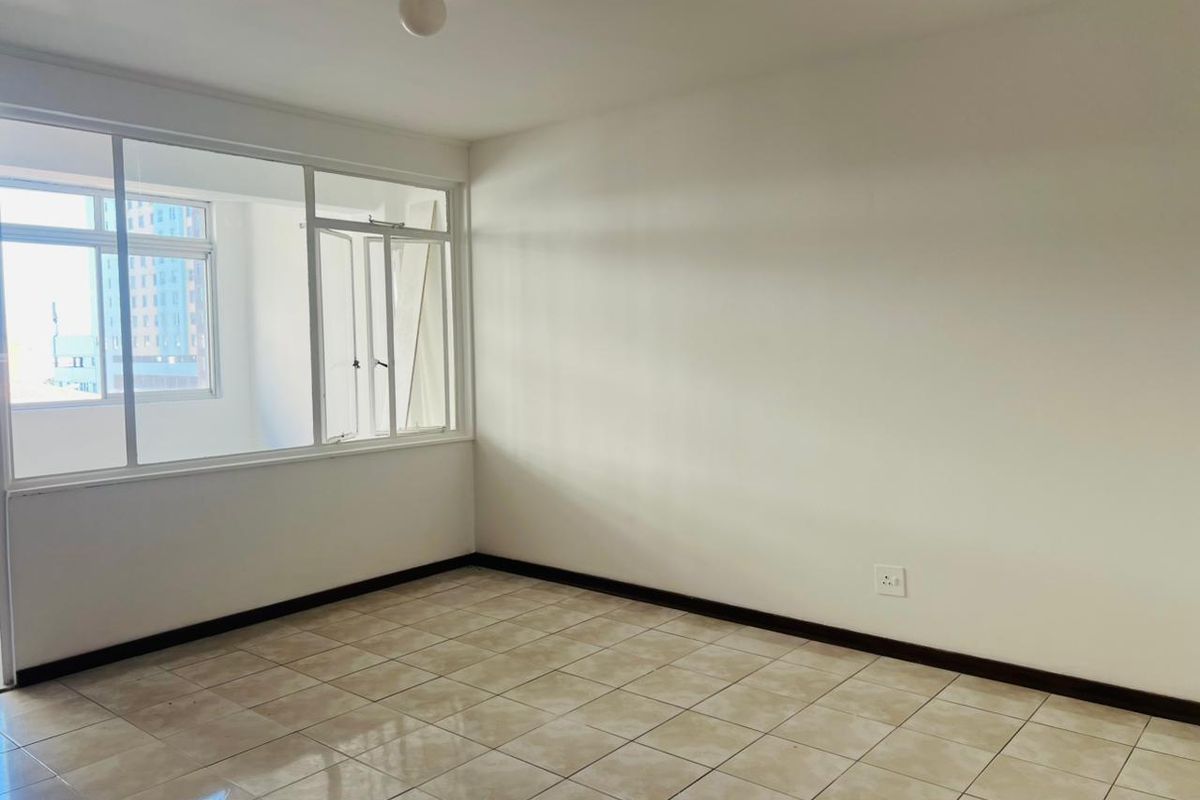 A bright, empty bedroom featuring neutral tiled flooring, white walls, and large windows providing natural light.
