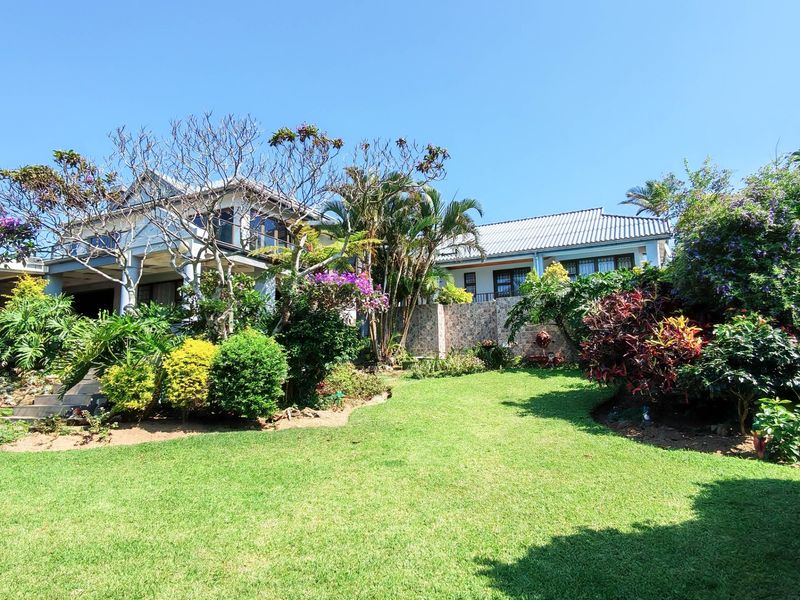 A well-maintained rear garden featuring lush landscaping, a stone-clad retaining wall, and a view of the home's covered patio and tiled roof structure.