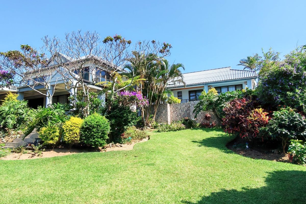 A well-maintained rear garden featuring lush landscaping, a stone-clad retaining wall, and a view of the home's covered patio and tiled roof structure.