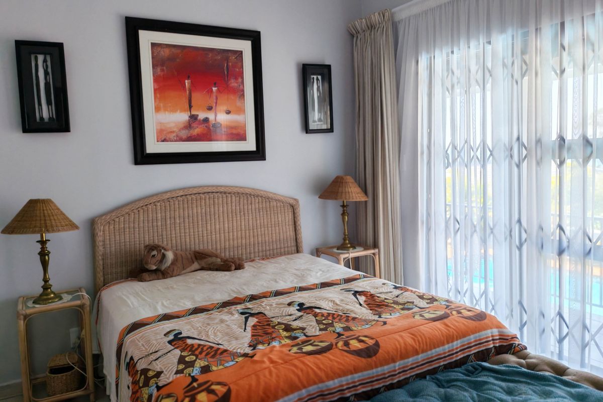 A well-maintained bedroom featuring neutral walls, a sliding glass door with security gate, and direct access to an outdoor area.
