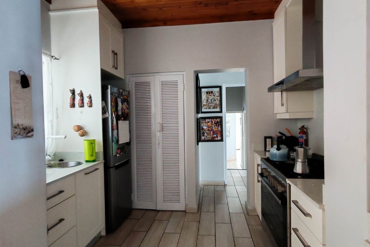 A functional kitchen featuring white cabinetry, stone countertops, a built-in oven with extractor fan, and a warm timber ceiling.