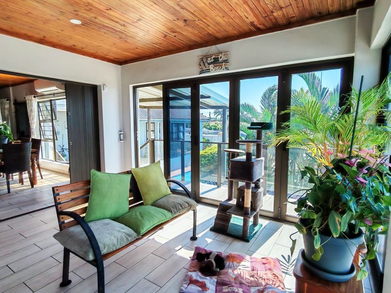 A bright living area featuring a warm timber-clad ceiling, tiled flooring, and large sliding doors that provide seamless access to the outdoor patio area.