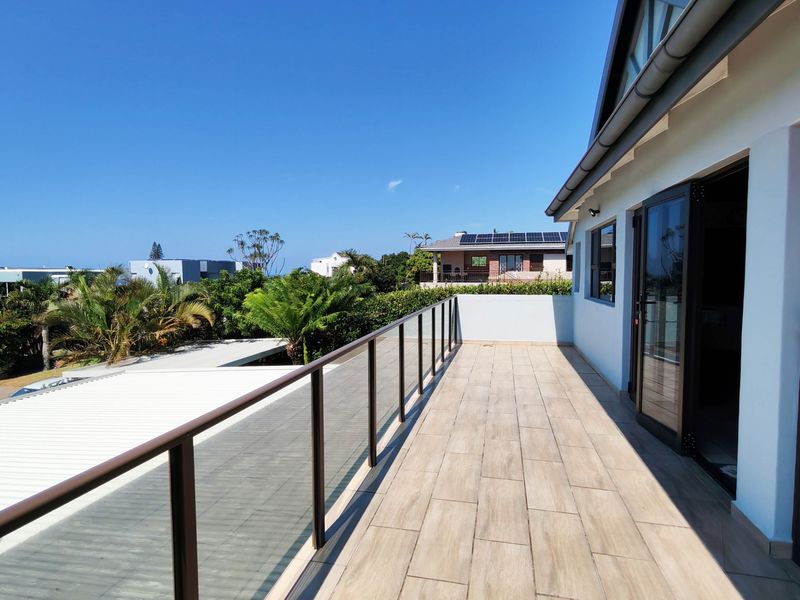 A spacious, modern balcony featuring a sleek glass balustrade, tiled flooring, and direct access to the interior through large sliding doors.