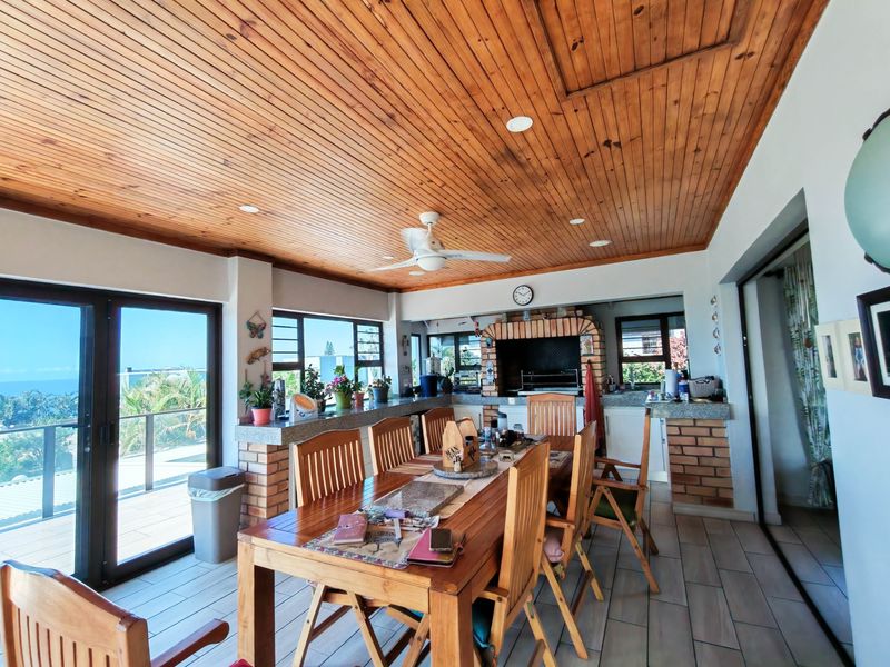 Spacious covered patio featuring a timber-clad ceiling, built-in brick braai, stone-topped breakfast bar, and direct access to an outdoor deck with sea views.