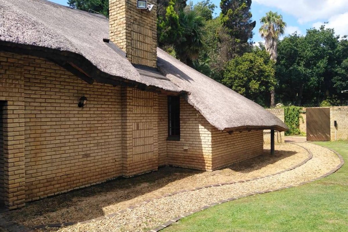 Rear view of a traditional face brick house featuring a thatched roof, brick chimney, and a gravel pathway surrounding the lawn.
