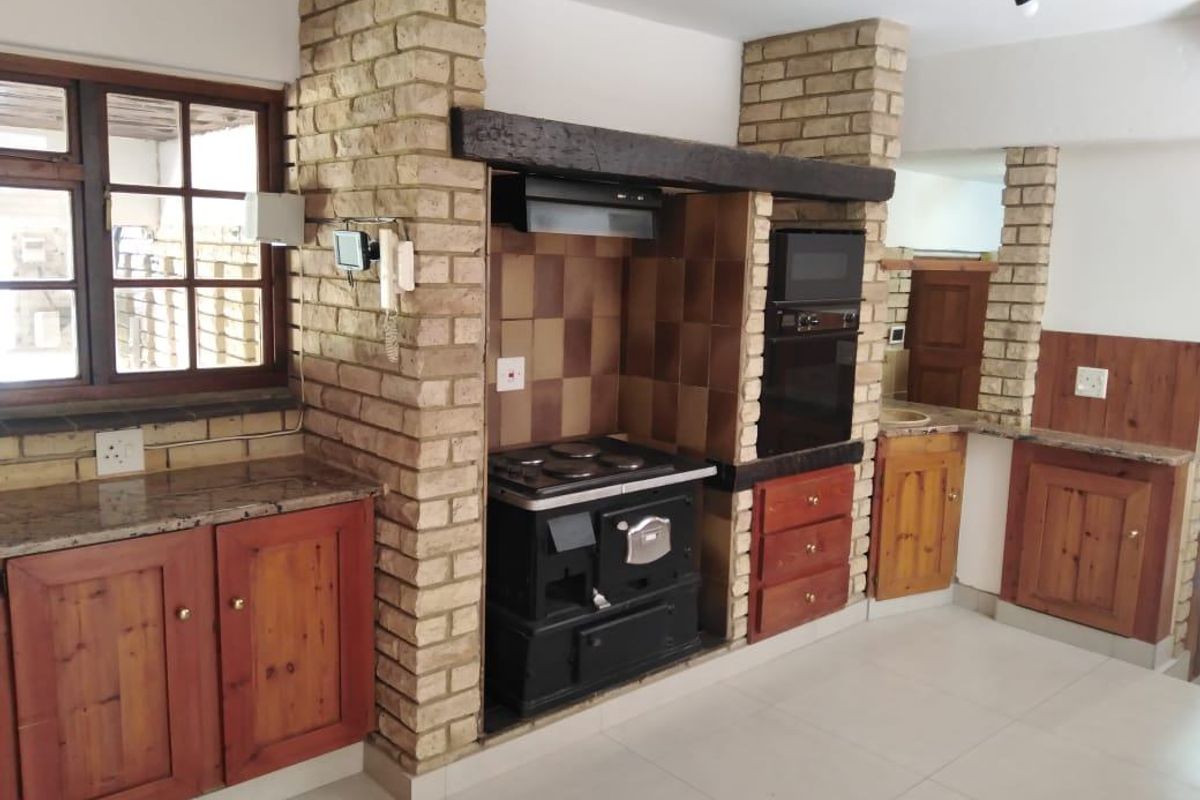 Rustic kitchen featuring exposed brick pillars, timber cabinetry, granite countertops, and a built-in oven with an electric hob.