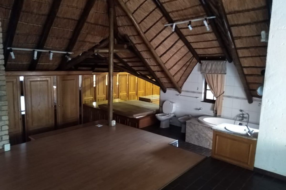 Spacious bedroom featuring a high thatched roof with exposed rafters, integrated bathroom fixtures including a bathtub and vanity, and extensive built-in wooden cabinetry.