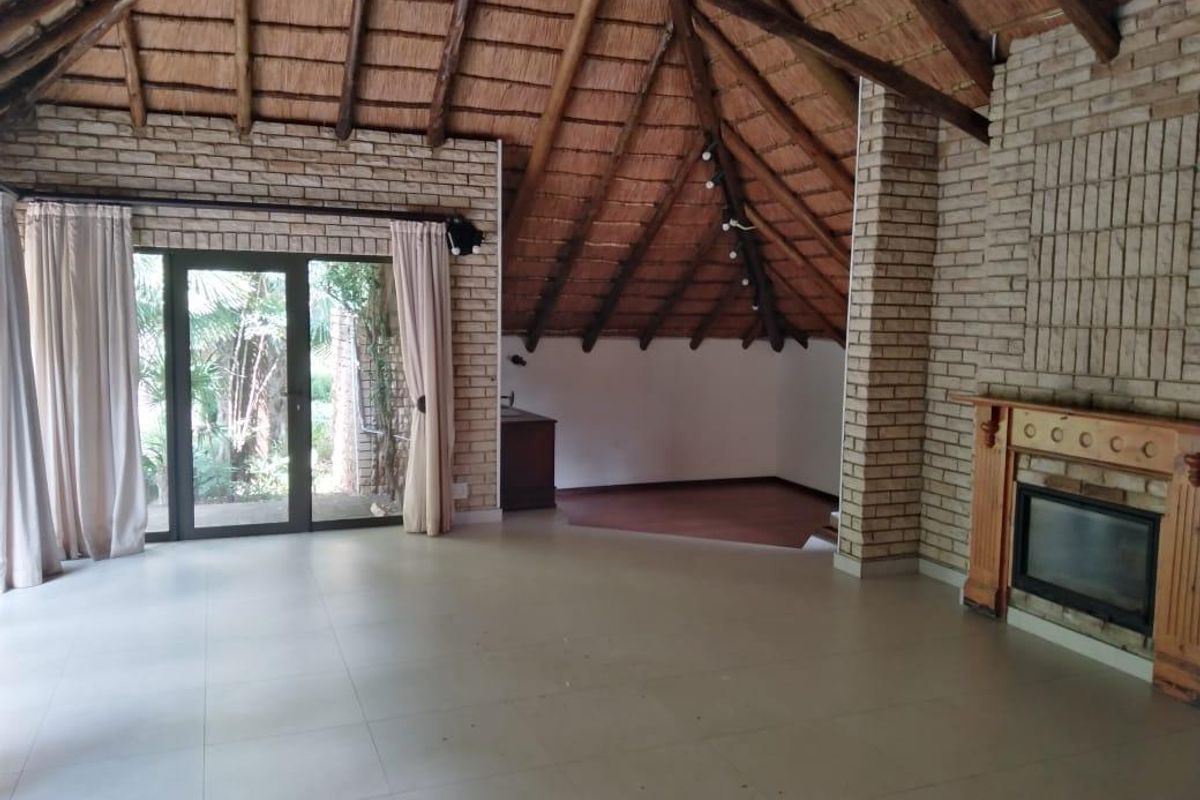 Spacious living area featuring a high thatched ceiling with exposed timber beams, exposed brick walls, a built-in fireplace, and large sliding doors to the garden.