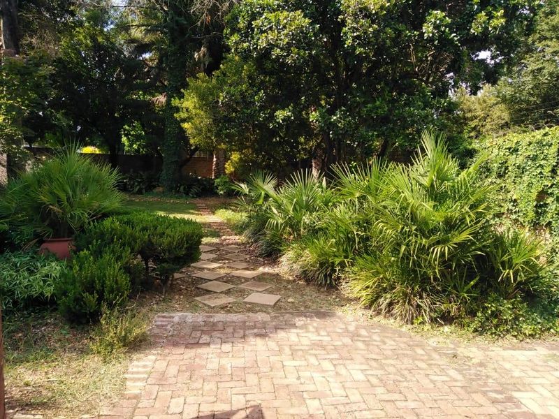 A lush, mature garden featuring brick paved pathways, stone stepping stones, and established trees and shrubs.