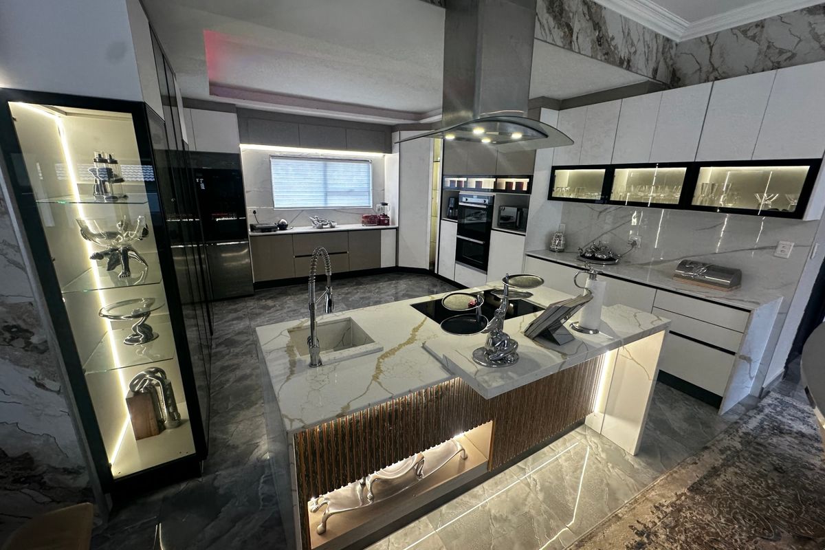 Modern luxury kitchen featuring a central island with stone countertops, integrated appliances, high-end cabinetry, and sophisticated ambient lighting throughout.