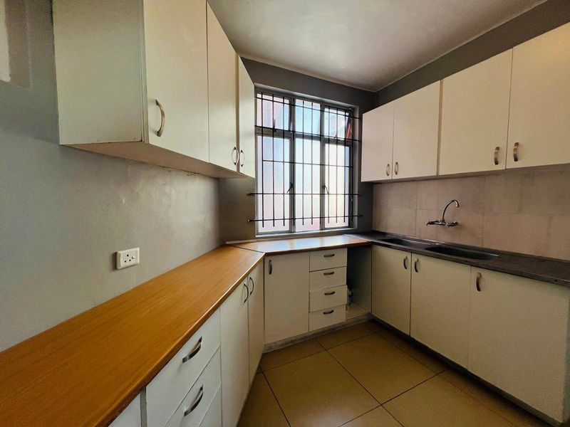 A functional kitchen featuring laminate countertops, ample built-in cabinetry, a stainless steel sink, and tiled flooring, offering a clean and practical workspace.