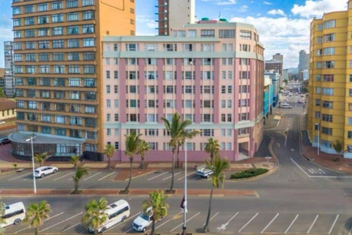 Aerial view of a multi-story apartment building situated on a corner lot with adjacent street parking and urban surroundings.
