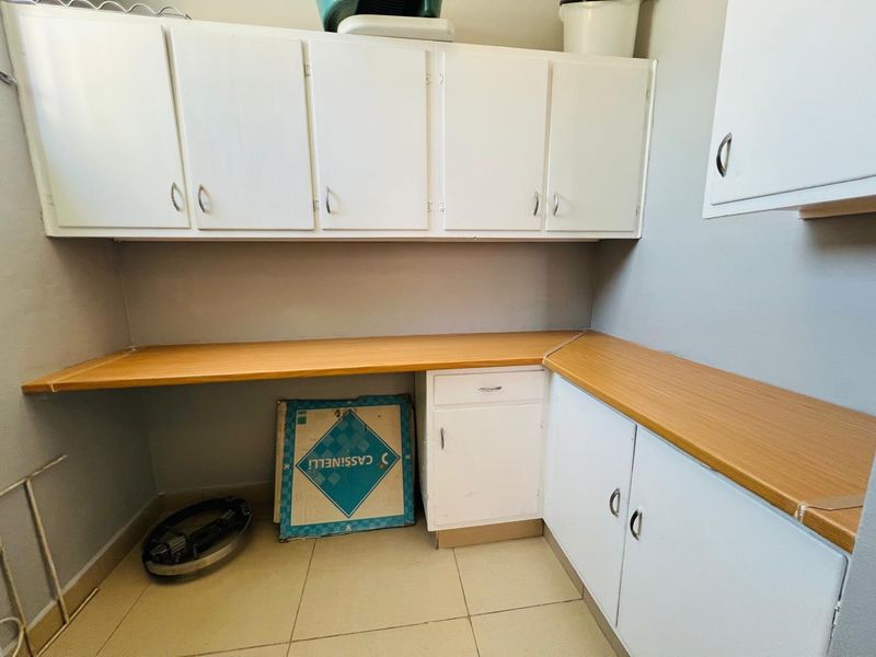 A functional laundry area featuring white built-in cabinetry, ample laminate countertop workspace, and neutral tiled flooring.