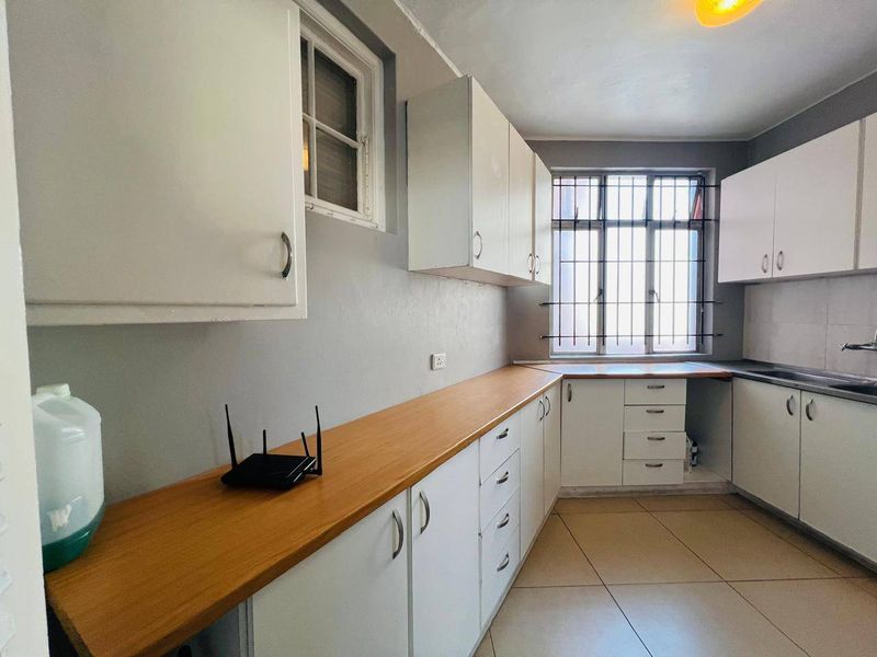 A functional kitchen featuring white cabinetry, laminate countertops, tiled flooring, and security bars on the windows.
