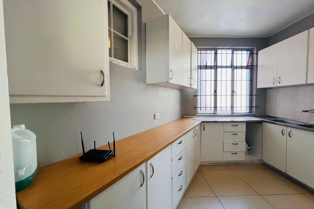 A functional kitchen featuring white cabinetry, laminate countertops, tiled flooring, and security bars on the windows.