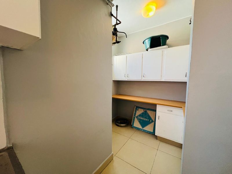 A functional laundry or utility space featuring built-in white cabinetry, a laminate countertop, and tiled flooring.